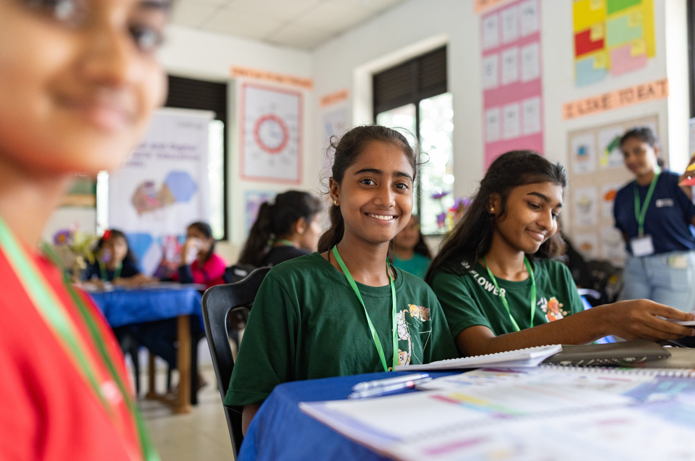 A girl in Sri Lanka sits at a desk, smiling.