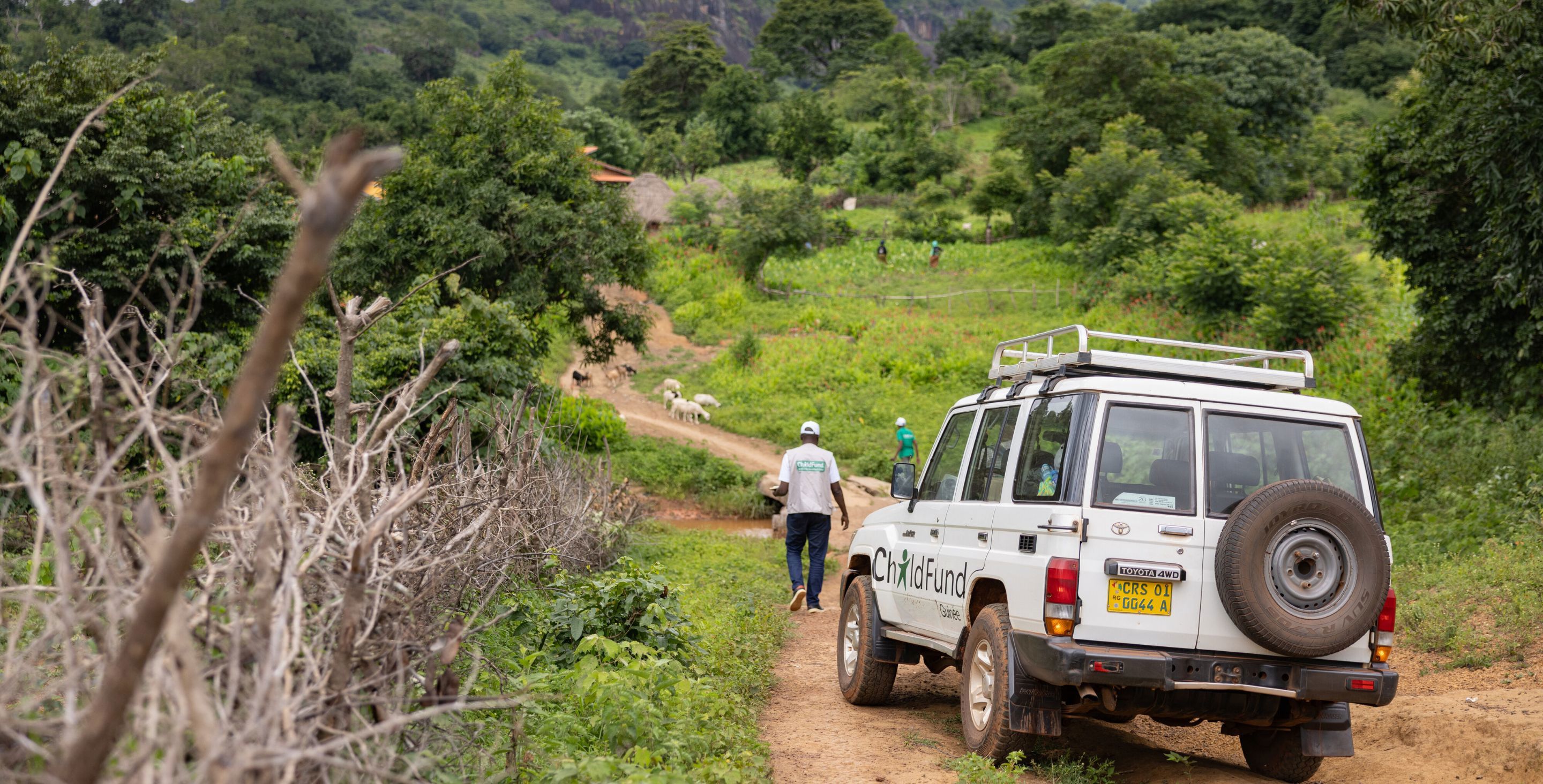 A ChildFund car rolls down a dirt road in a rural community.