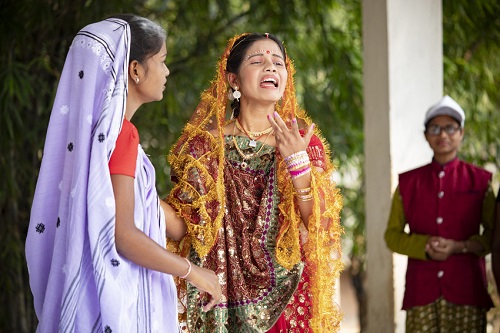 Teen in red bridal dress cries dramatically as part of a street play about child marriage.