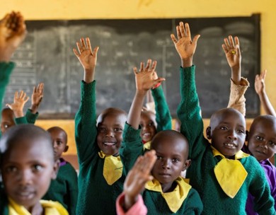 Students smile and raise their hands in their classroom