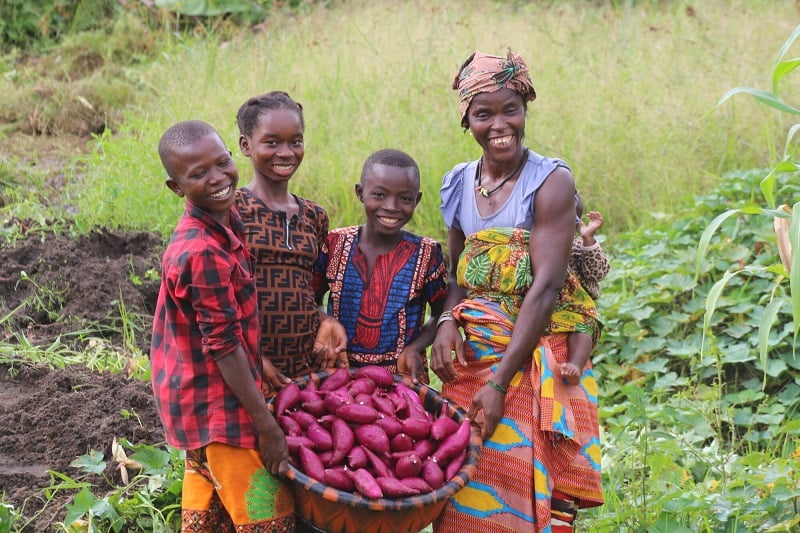 Family smiles holding their sweet potato harvest in Sierra Leone.