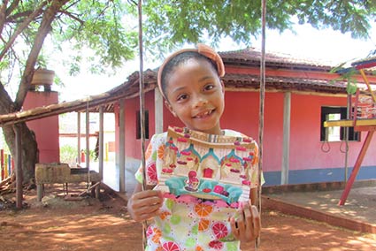Sponsored child in Brazil sits outside on a swing holding a letter, smiling.