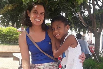 Woman and child sitting outdoors, hugging, smiling.