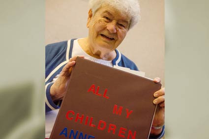 Woman sitting indoors smiling holding a book titled All My Children.