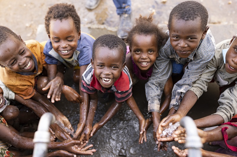 Kids wash their faces at a well, looking at camera and smiling.
