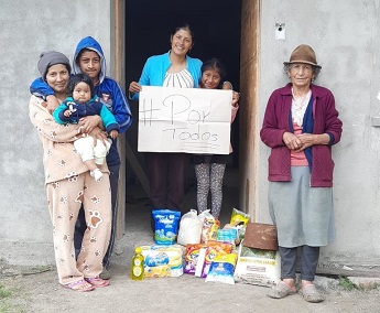 Family standing in doorway holding sign with food and soap in Ecuador.