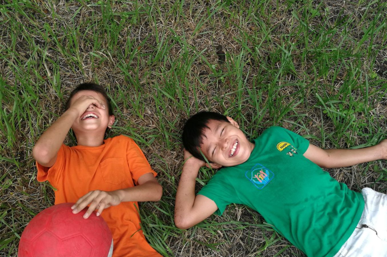 Two boys lay in the grass laughing in Honduras, one of them holding a soccer ball.