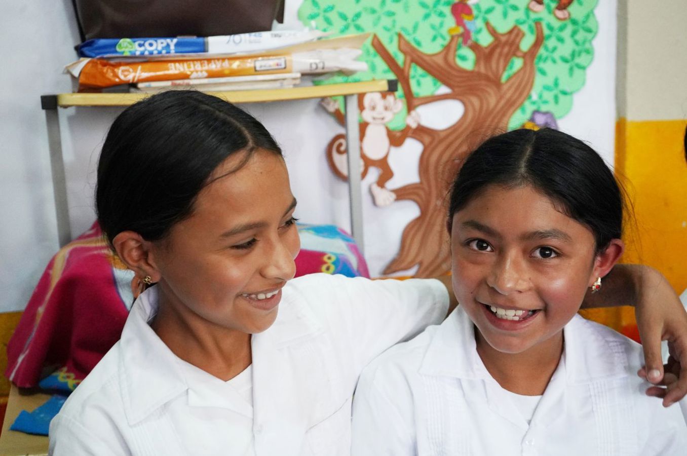 Two school-age girls in Honduras laugh together, wearing white uniforms.