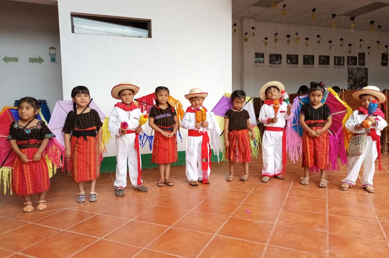 Small children wearing traditional colorful clothing stand in a line, looking at the camera.