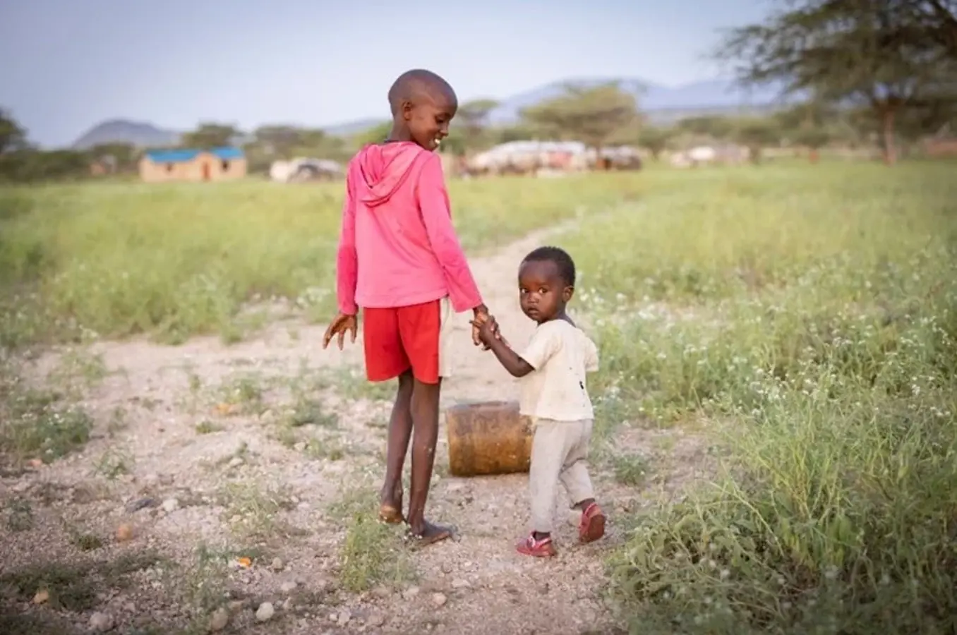 A young girl walks with her brother through a field.