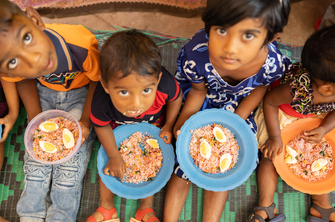 Children in Sri Lanka sit on the ground, eating and looking up at the camera