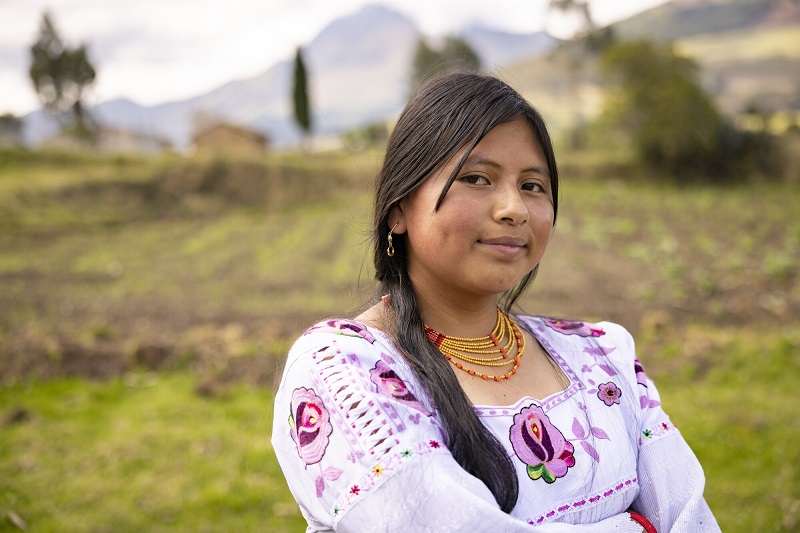 A teen girl in Ecuador looks somberly at the camera with folded arms, slightly smiling.