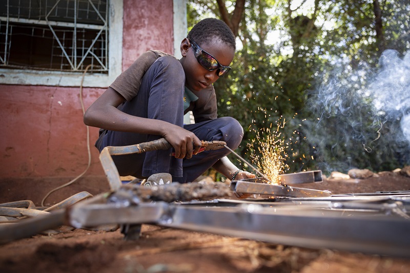A teen boy in Kenya makes sparks fly as he welds, goggles on.