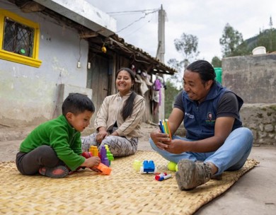 Smiling ECD student and ChildFund staff member play with blocks outside 