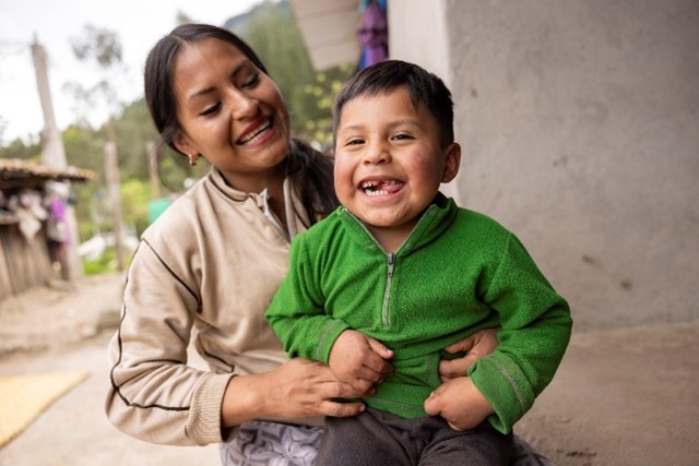 A mother holds a smiling boy in her lap.