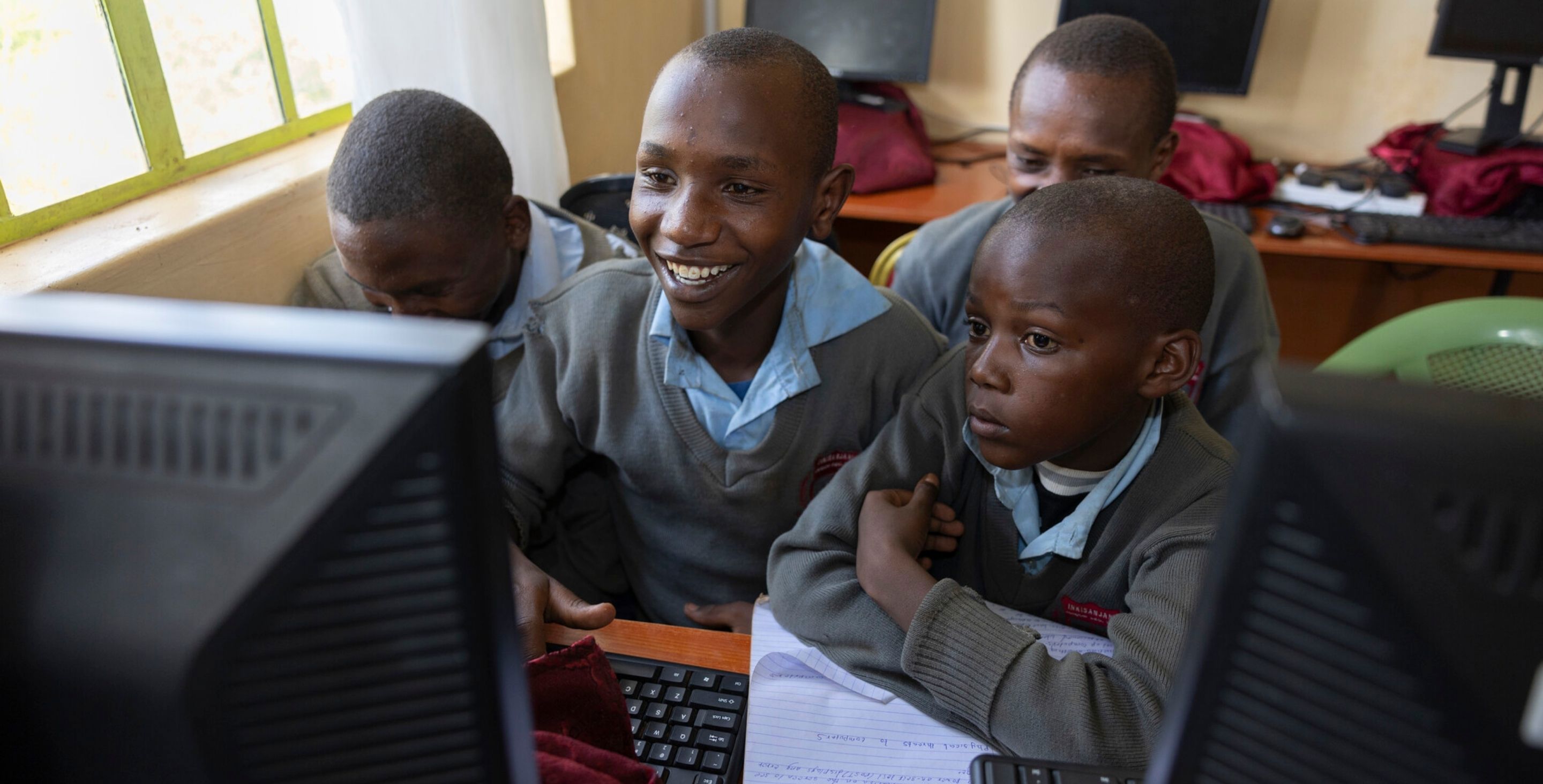 Teens in Kenya gather around a computer in a computer lab.