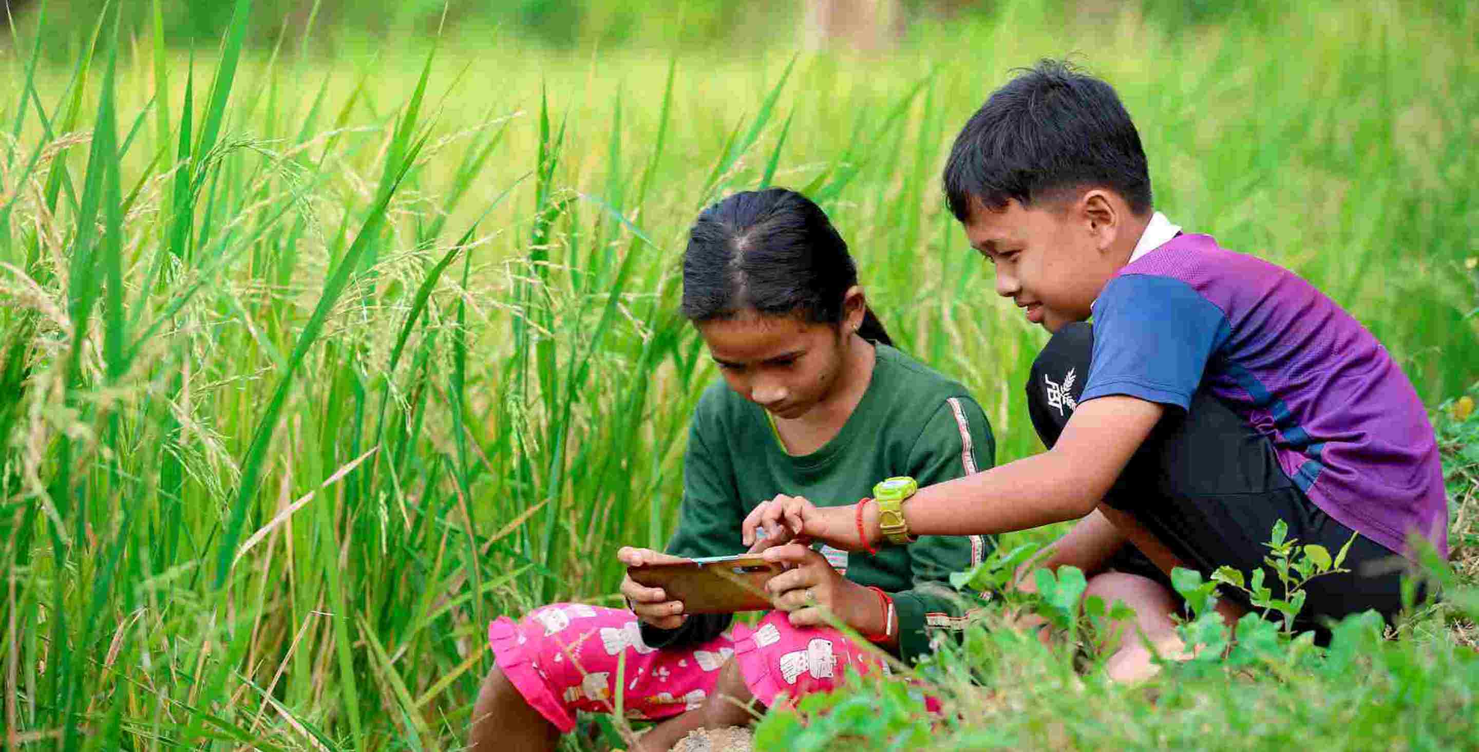 two children sitting in grass and looking at a tablet together