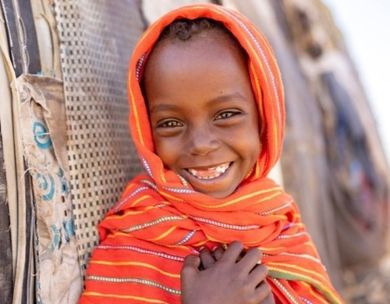 A young girl in an orange shawl smiles.
