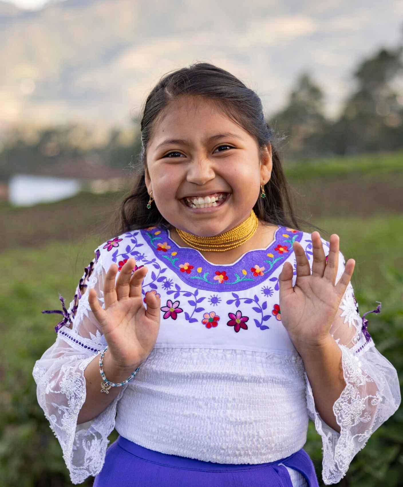 A girl in Ecuador smiles against a lush green backdrop.