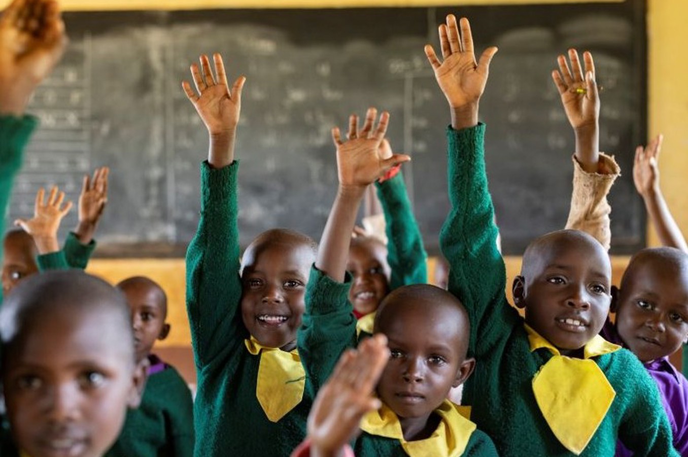 Children in a recently renovated classroom raise their hands and smile.
