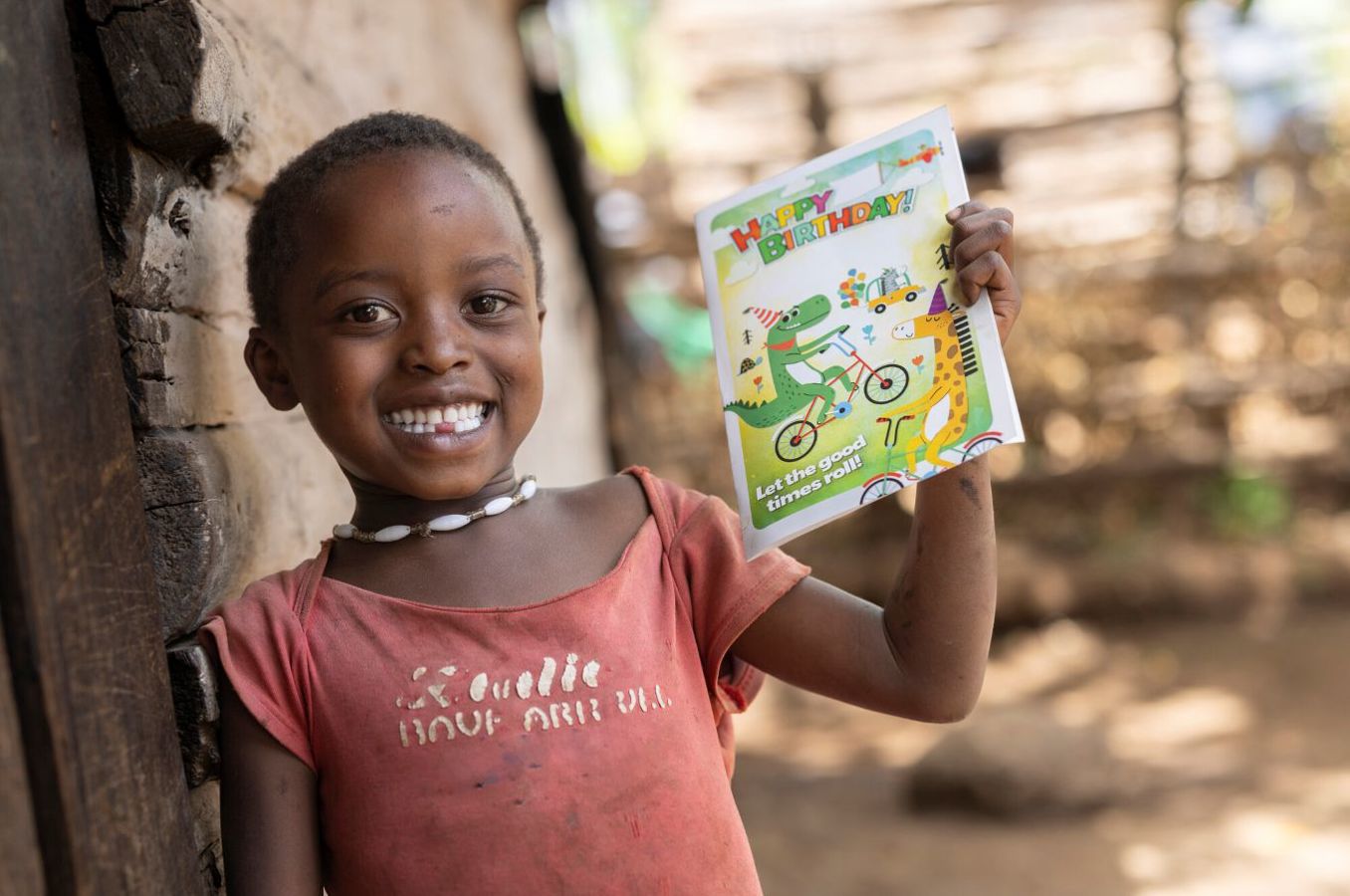 A little girl in Kenya holds up a colorful birthday card, smiling widely.