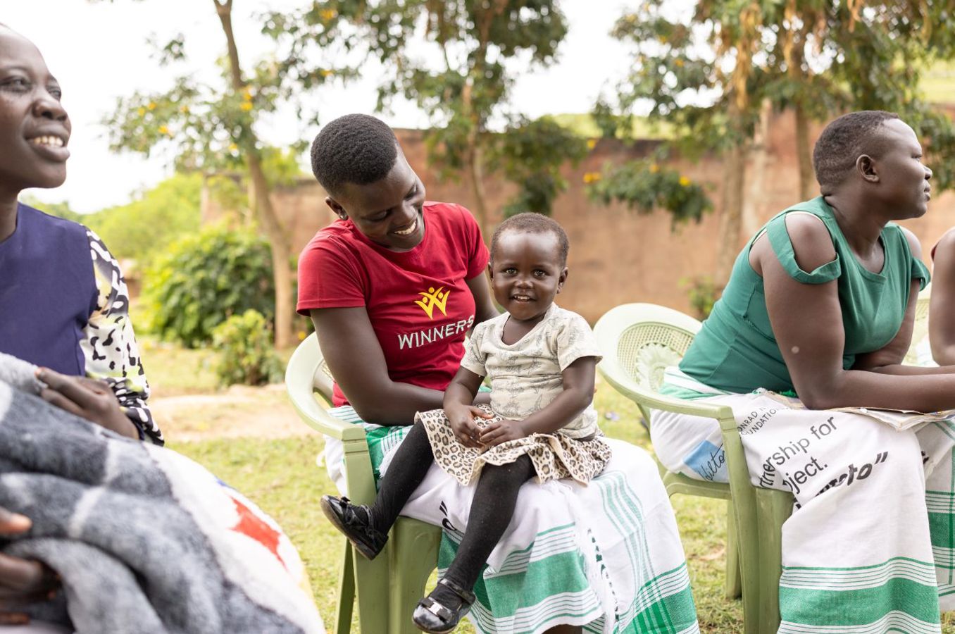 A mother in Kenya seated in a plastic chair holds a smiling baby.