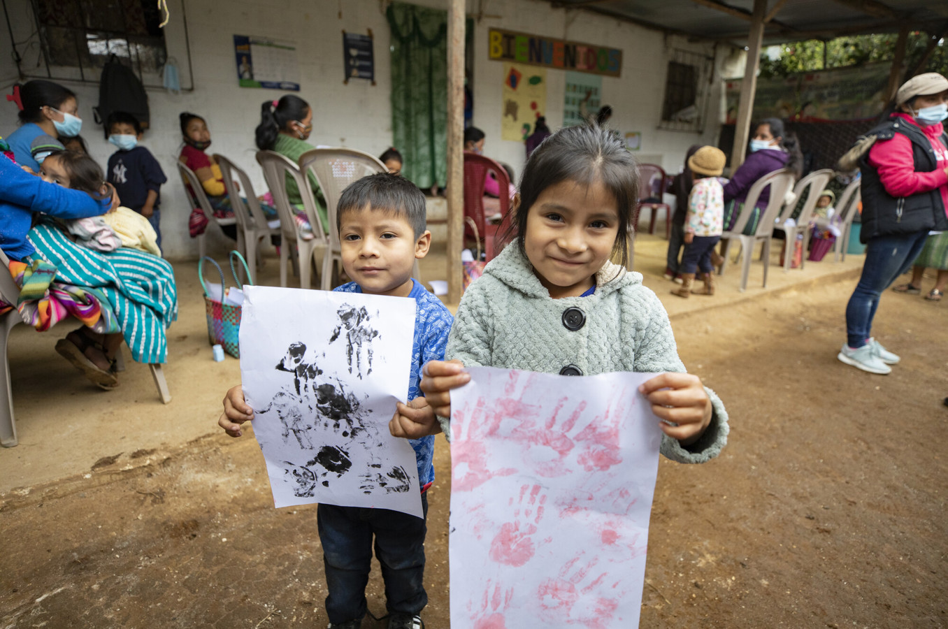 Two children in Guatemala hold up drawings they made out of their handprints.