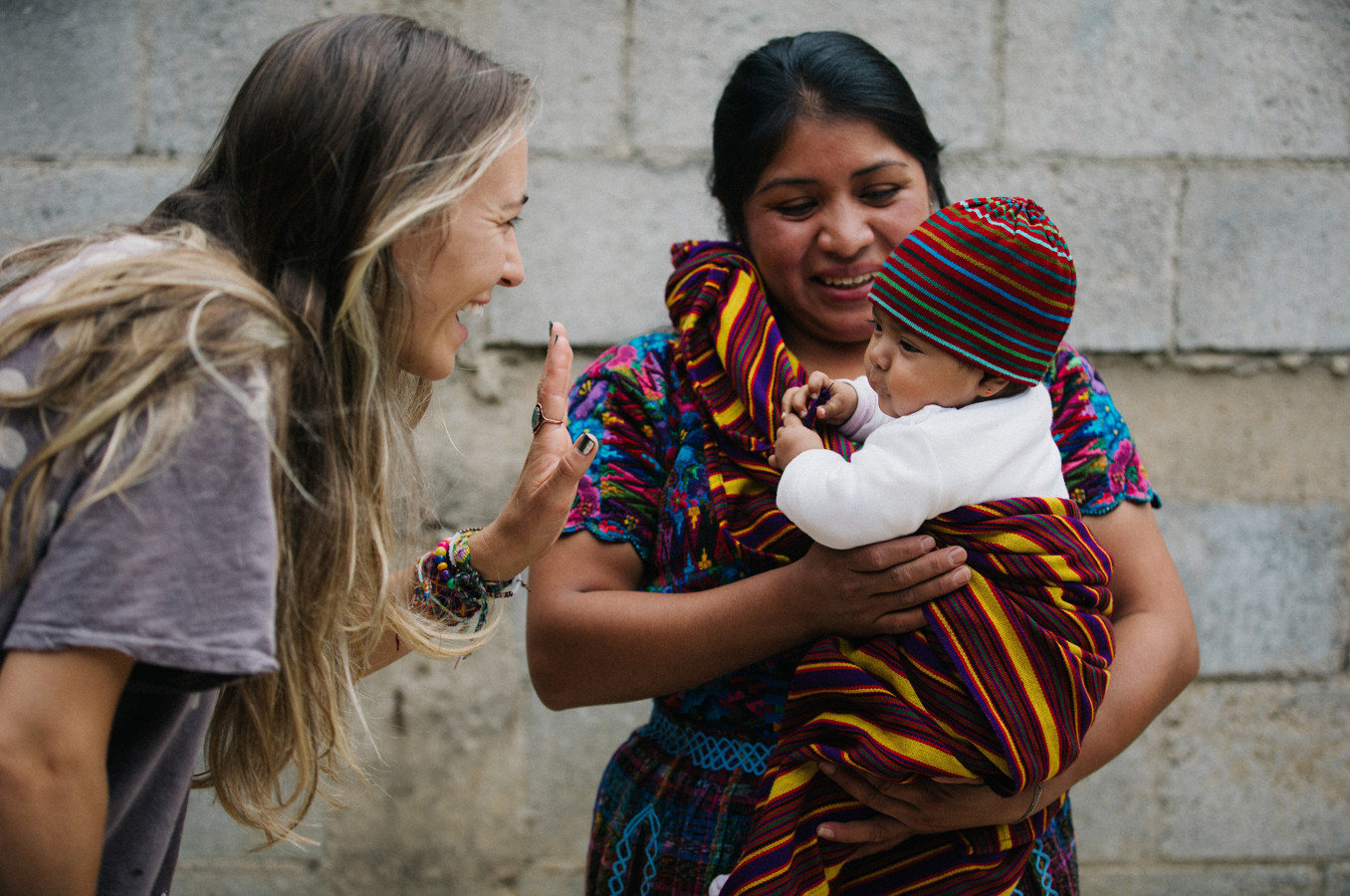 Singer Lauren Daigle smiles and waves at a baby on a smiling woman's back in Guatemala.