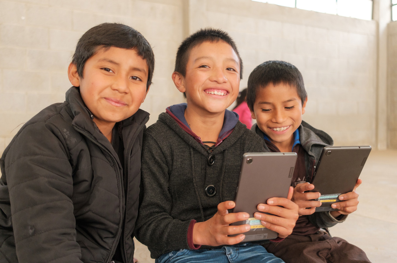 Three boys in Guatemala smile while using tablets.