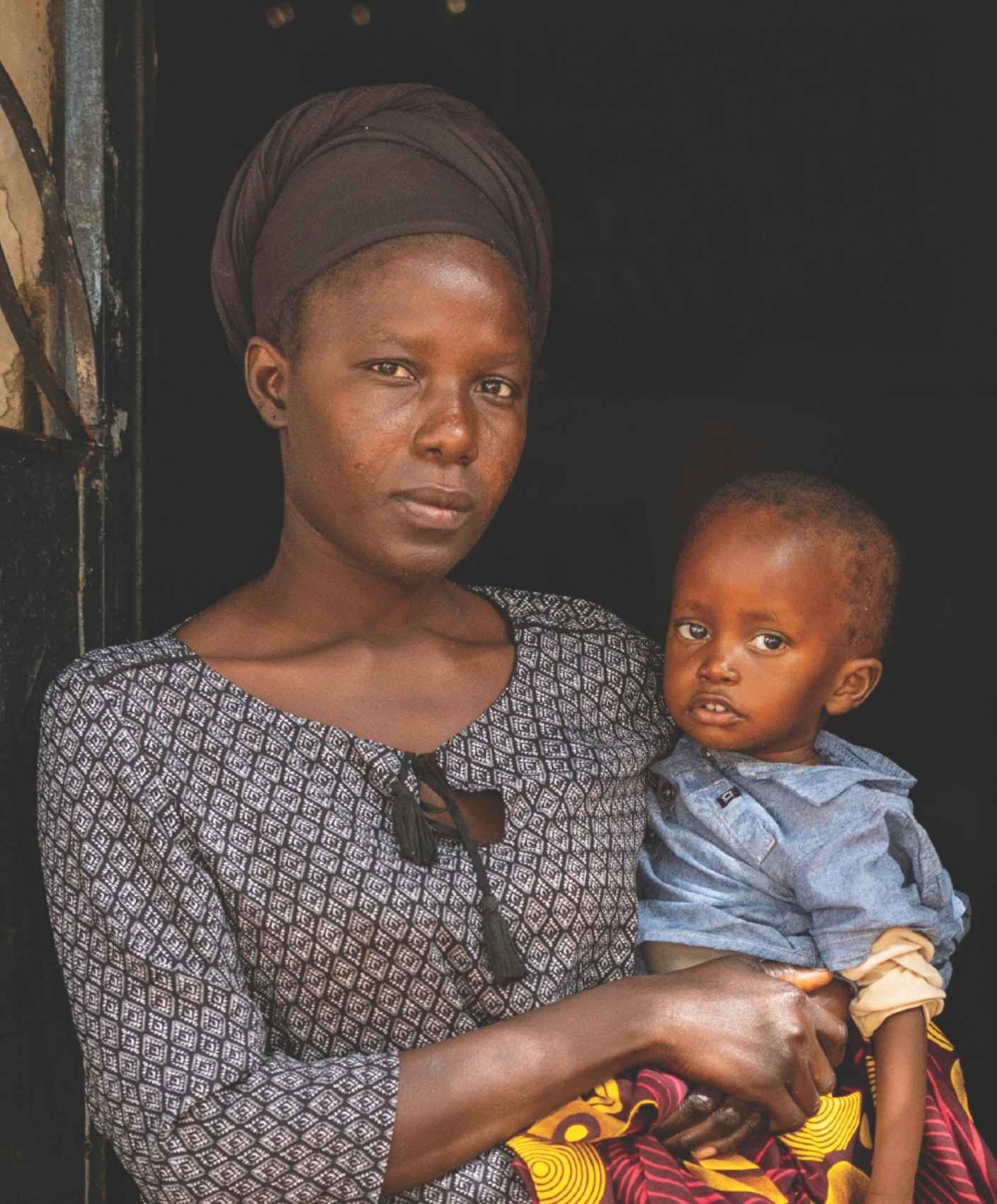 Woman looks seriously at camera while holding child outside of home
