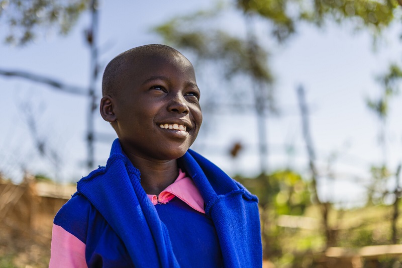 A Kenyan girl in a blue and pink school uniform pauses to smile.