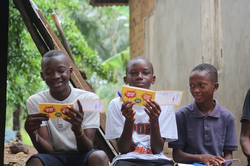 Boys in Sierra Leone smile while reading correspondence from their sponsors.