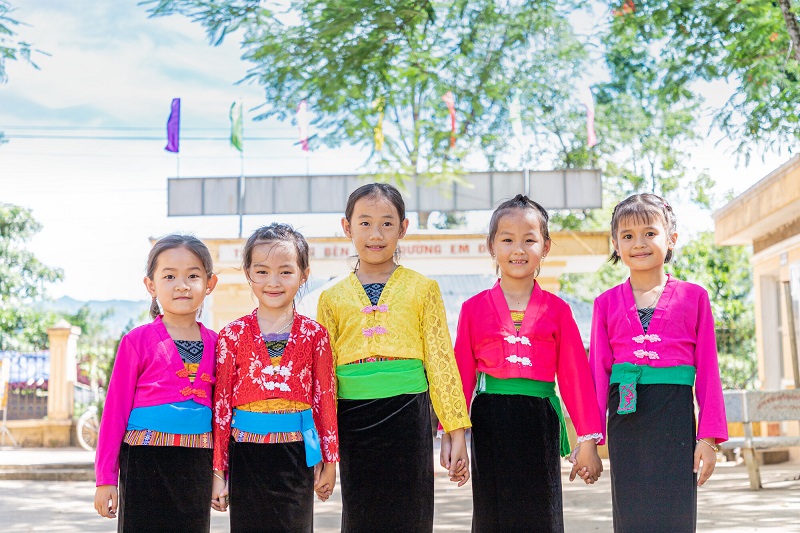Girls in Vietnam dressed in bright colors hold hands and smile.