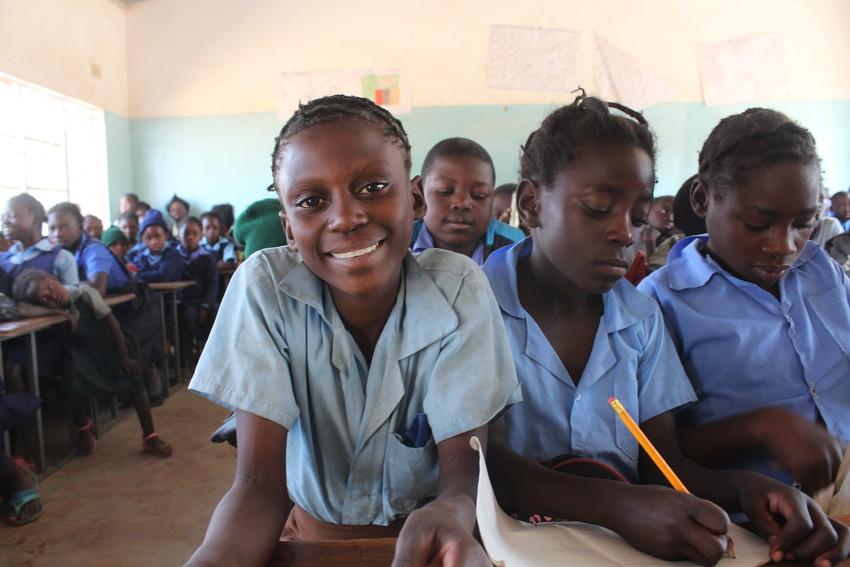August 15, 2019, An 11-year-old girl stands in front of a hut with a thatched roof in Zambia, looking at the camera.