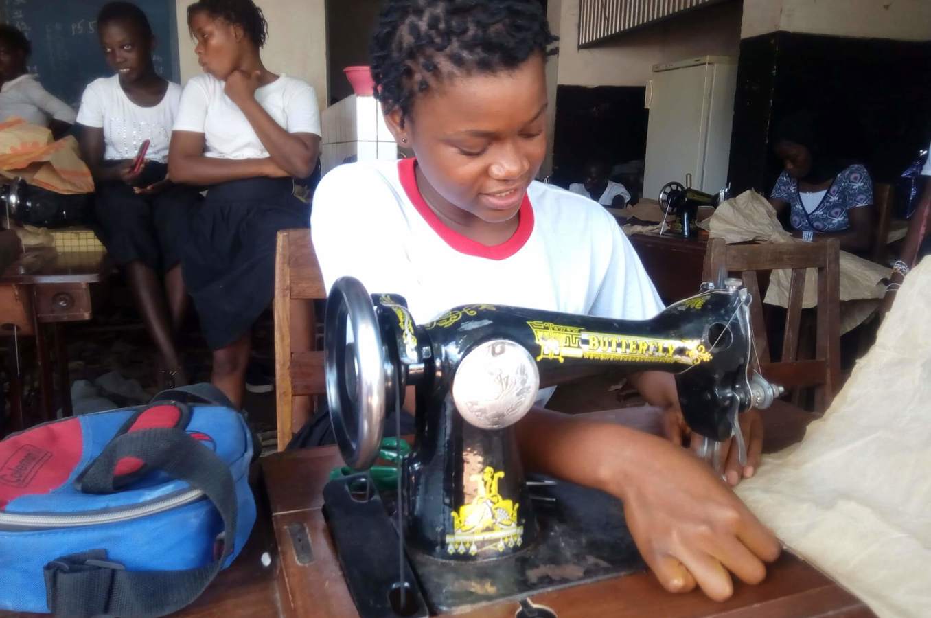 A young girl in Guinea sits at a table using a sewing machine.