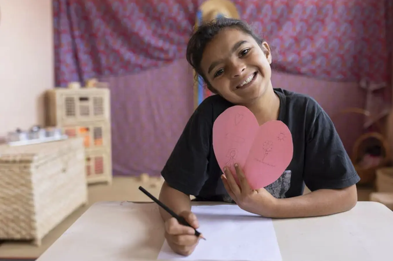 A young girl smiles while holding up a heart shaped card.