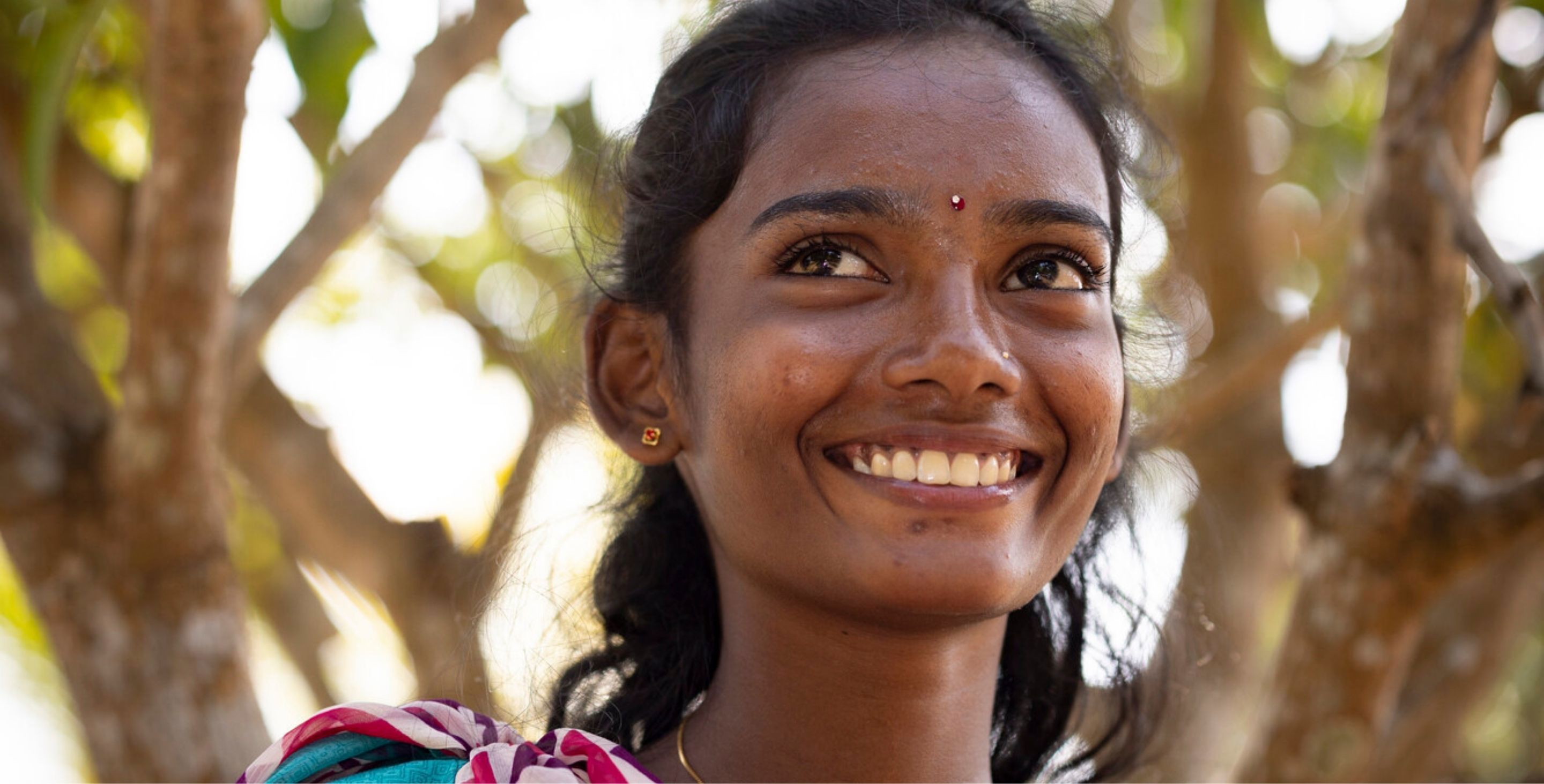 A young woman in Sri Lanka smiles outdoor beneath a set of trees.
