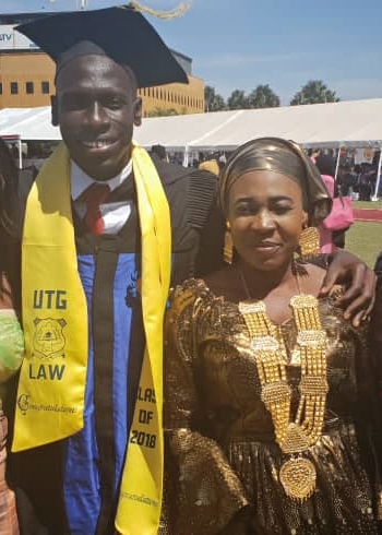 A young man wearing graduation cap and gown and his mother stand outside in the Gambia, smiling.