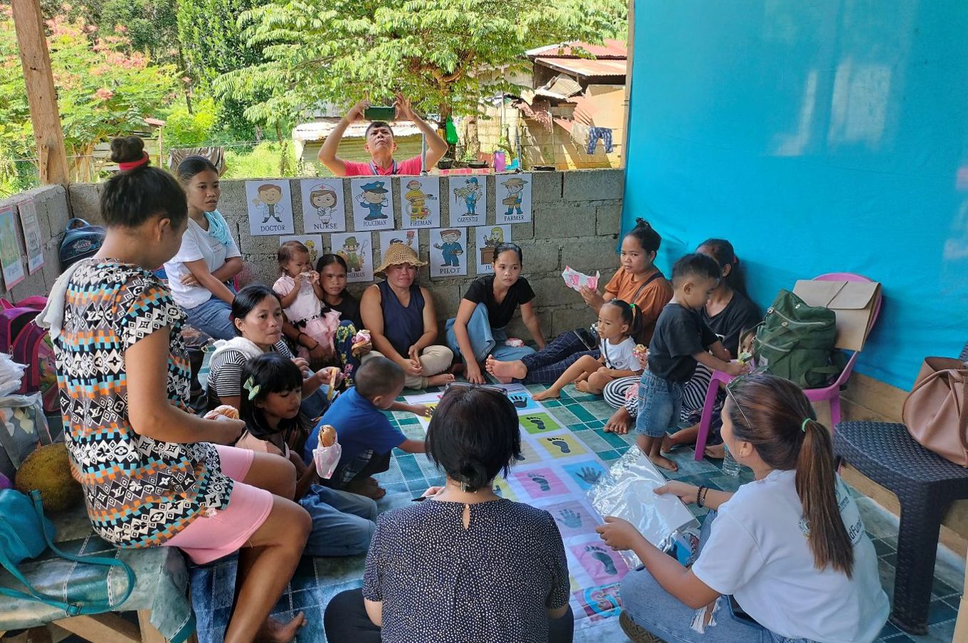 A group of parents with small children sit in a circle on an outdoor patio in the Philippines.