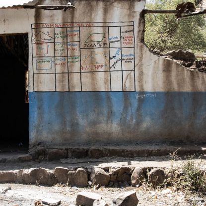 A girl in Ethiopia stands facing a former school building that has been destroyed in a war, her back to the camera.