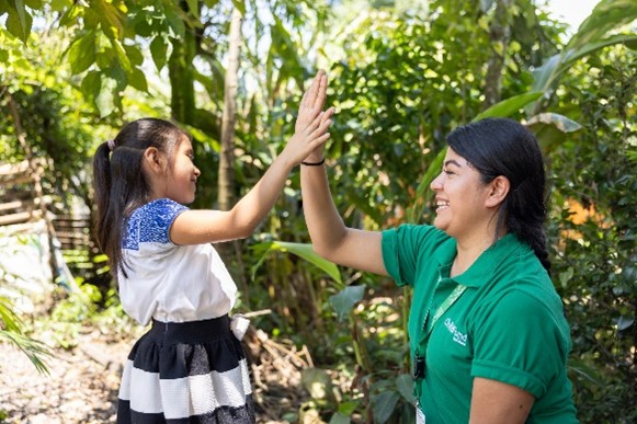 A child and an adult giving a high-five outdoors in a lush, green setting.