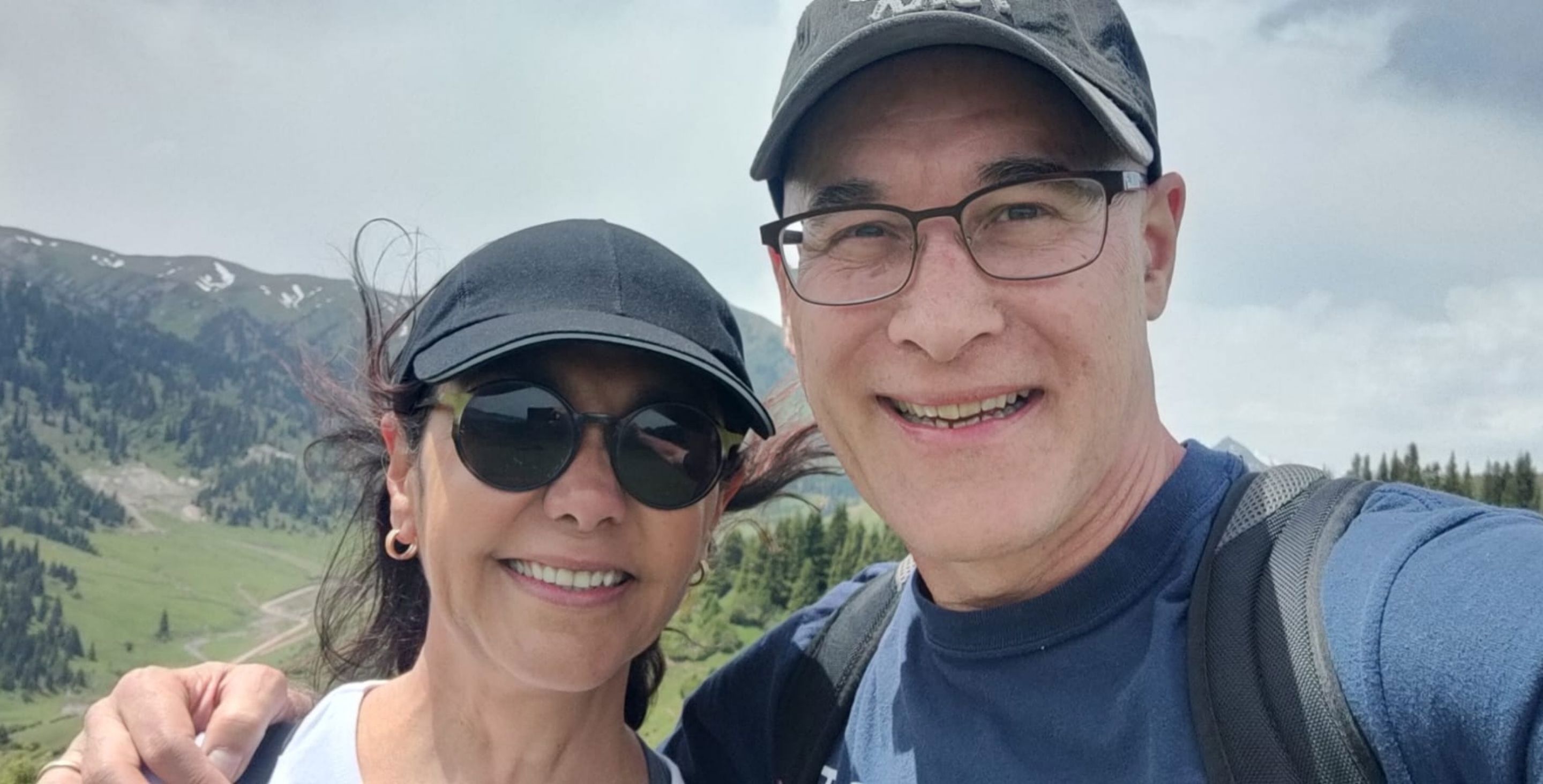 A man and woman stand on top of a mountain taking a selfie.