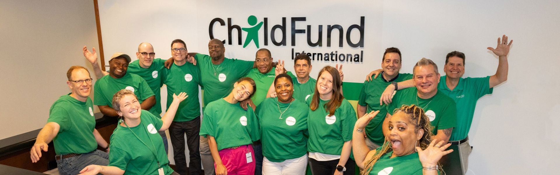 A group of employees wearing ChildFund shirts pose for a photo in front of a sign that reads 