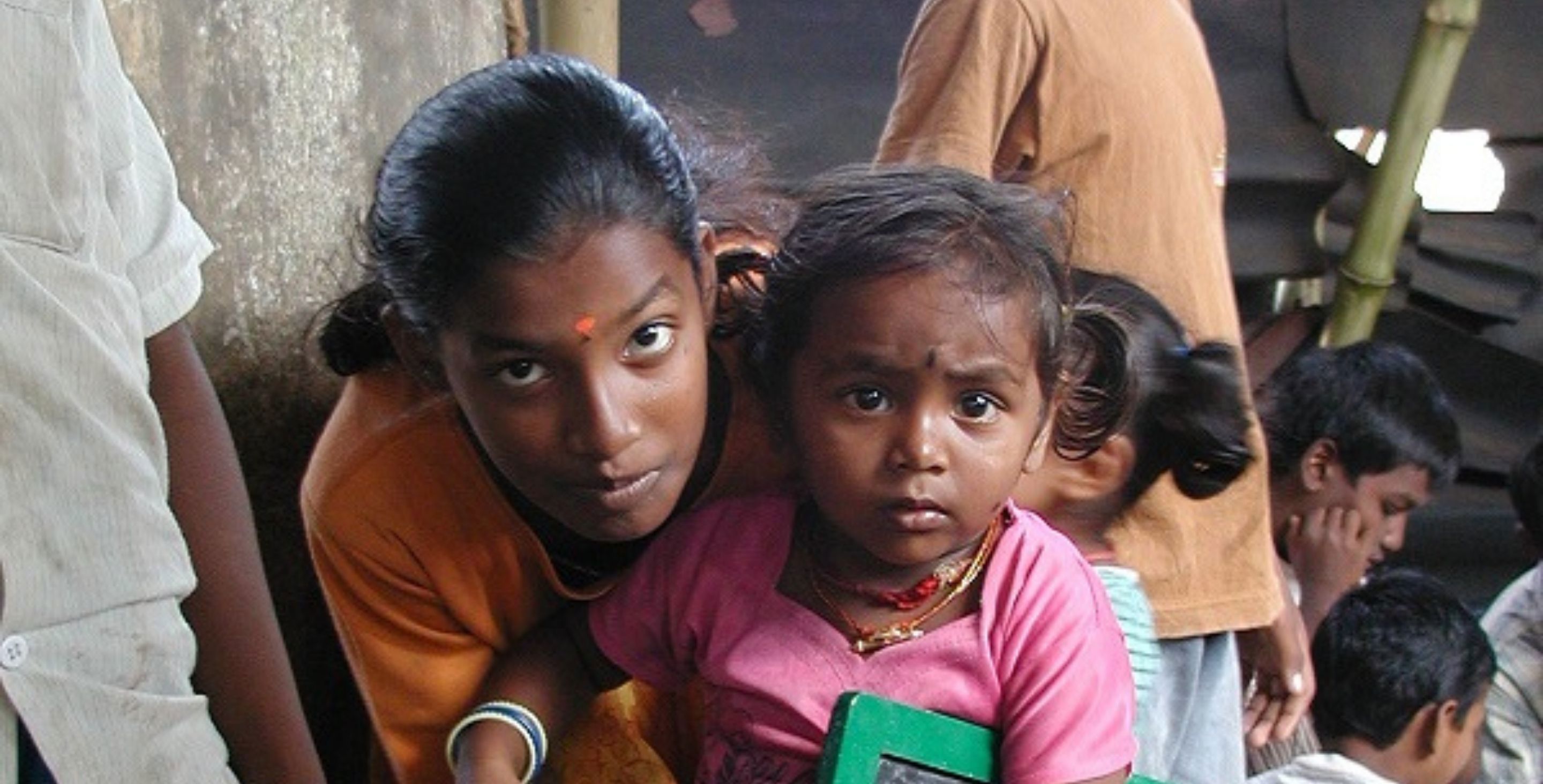 A mother and young girl crouch in an emergency shelter in Sri Lanka, looking somberly at the camera.