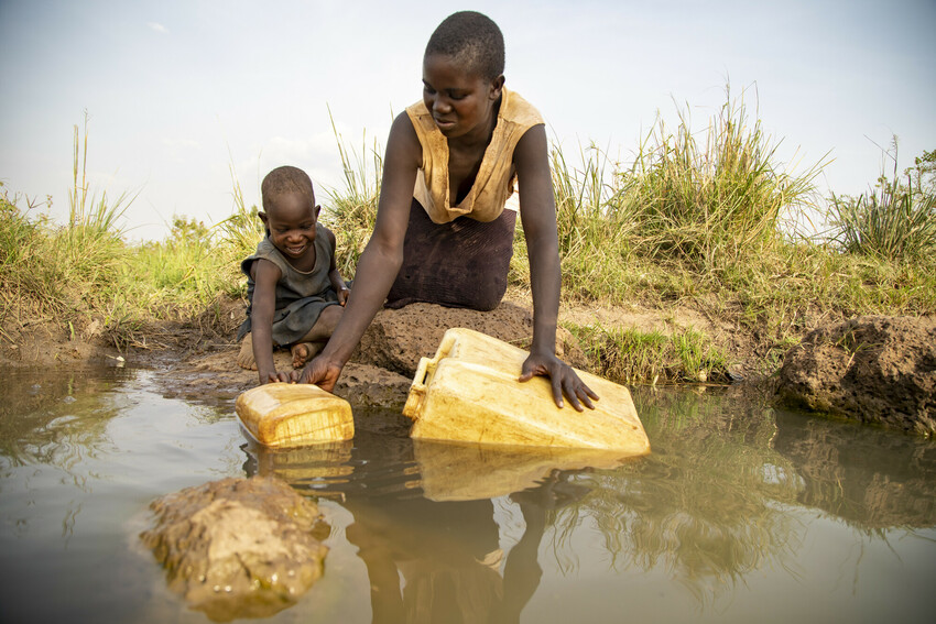 Young girl and her mom in Uganda gather water from a dirty pond.