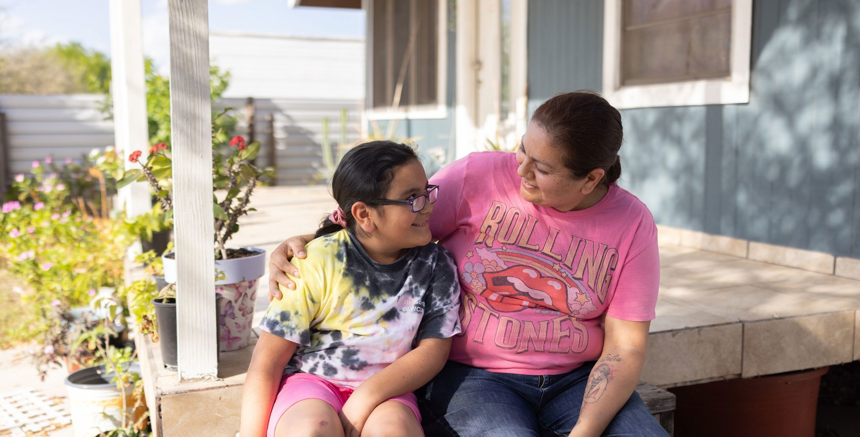 A mom and her daughter sit on a porch in Rio Grande Valley, Texas, hugging.