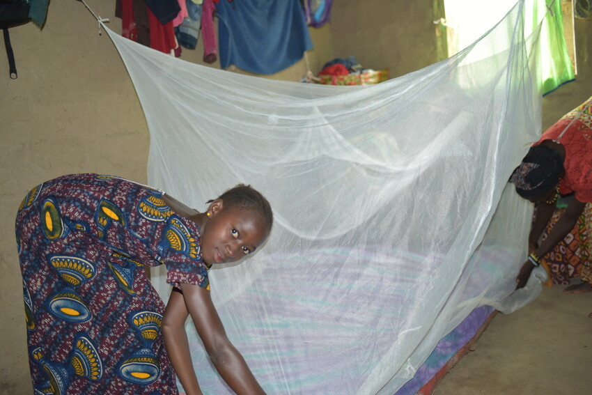 A young girl spreads a mosquito net on her bed in Sierra Leone.