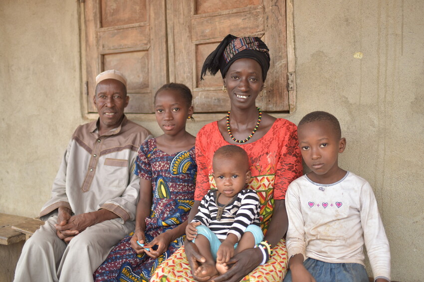 A family sits smiling in front of their home in Sierra Leone.