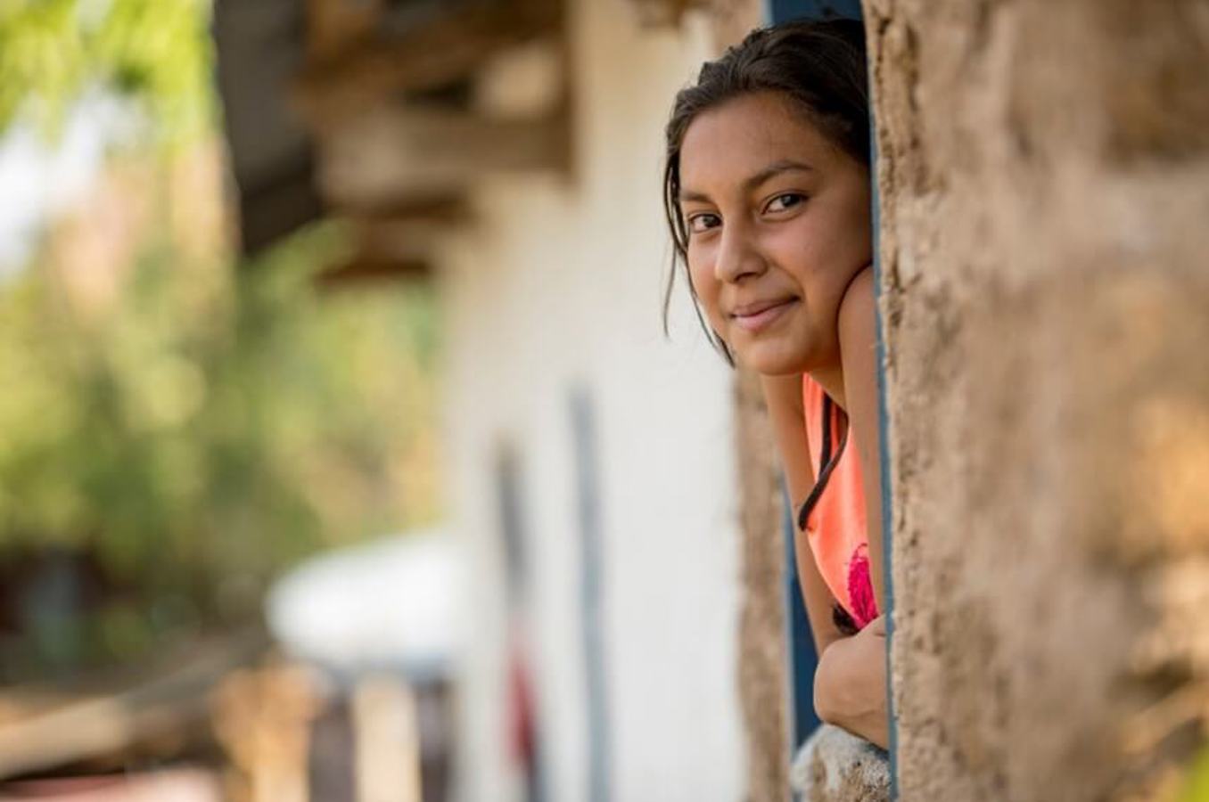 Young woman peeks out a window and smiles