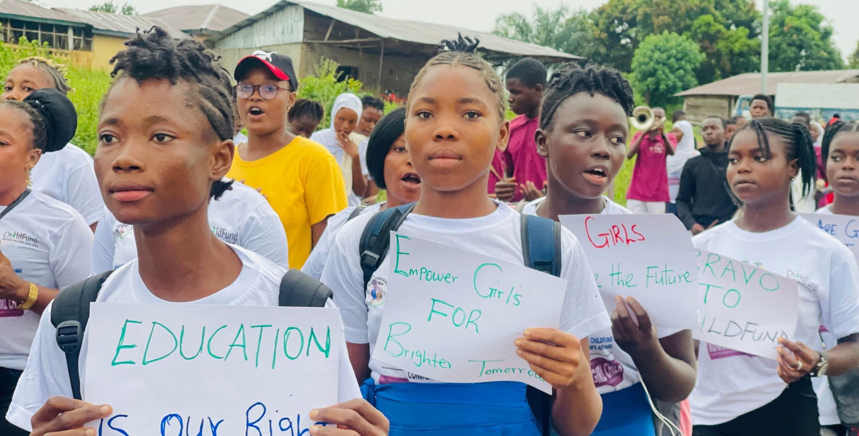 Schoolgirls in Sierra Leone march in parade, holding signs that read 